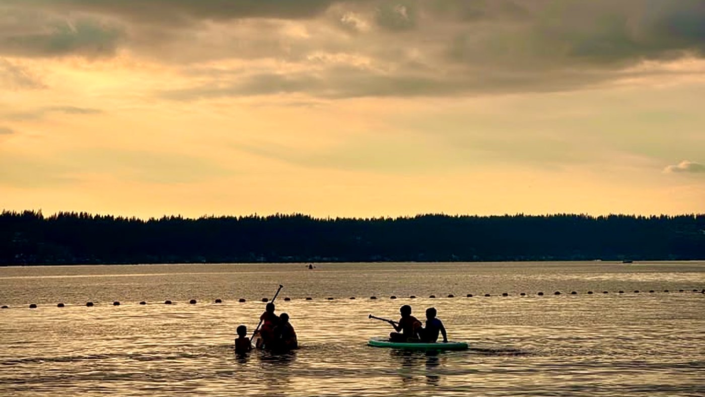 Scouts swimming and paddleboarding on Lake Sammamish at sunset, seen as silhouettes against the water.